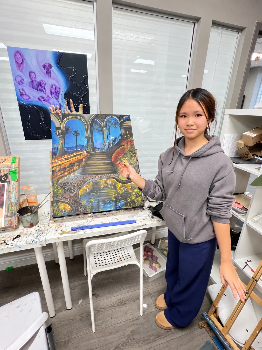 Mia standing beside one of her paintings, an arched nighttime courtyard scene