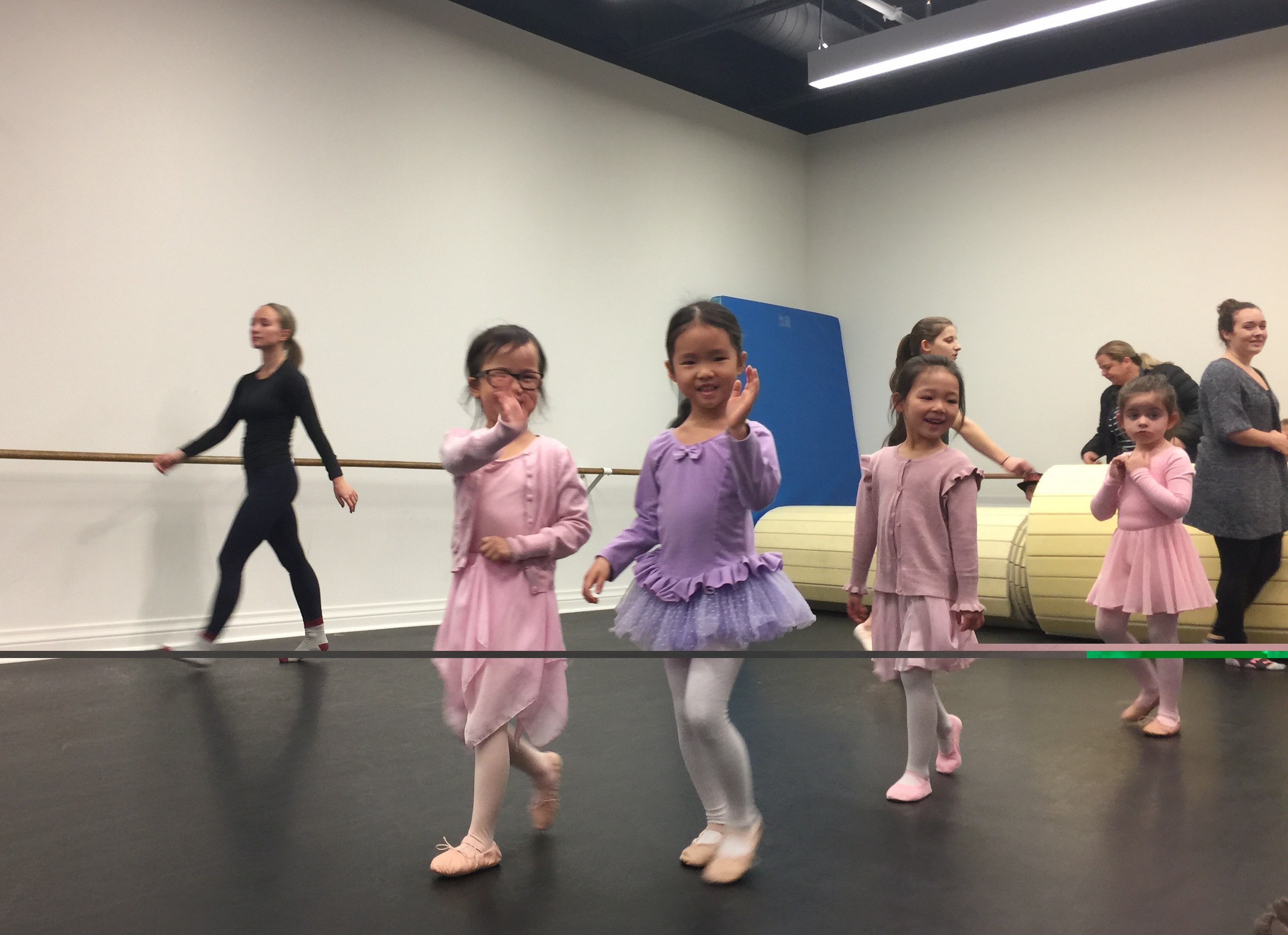 A young Mia waving and smiling during a ballet class