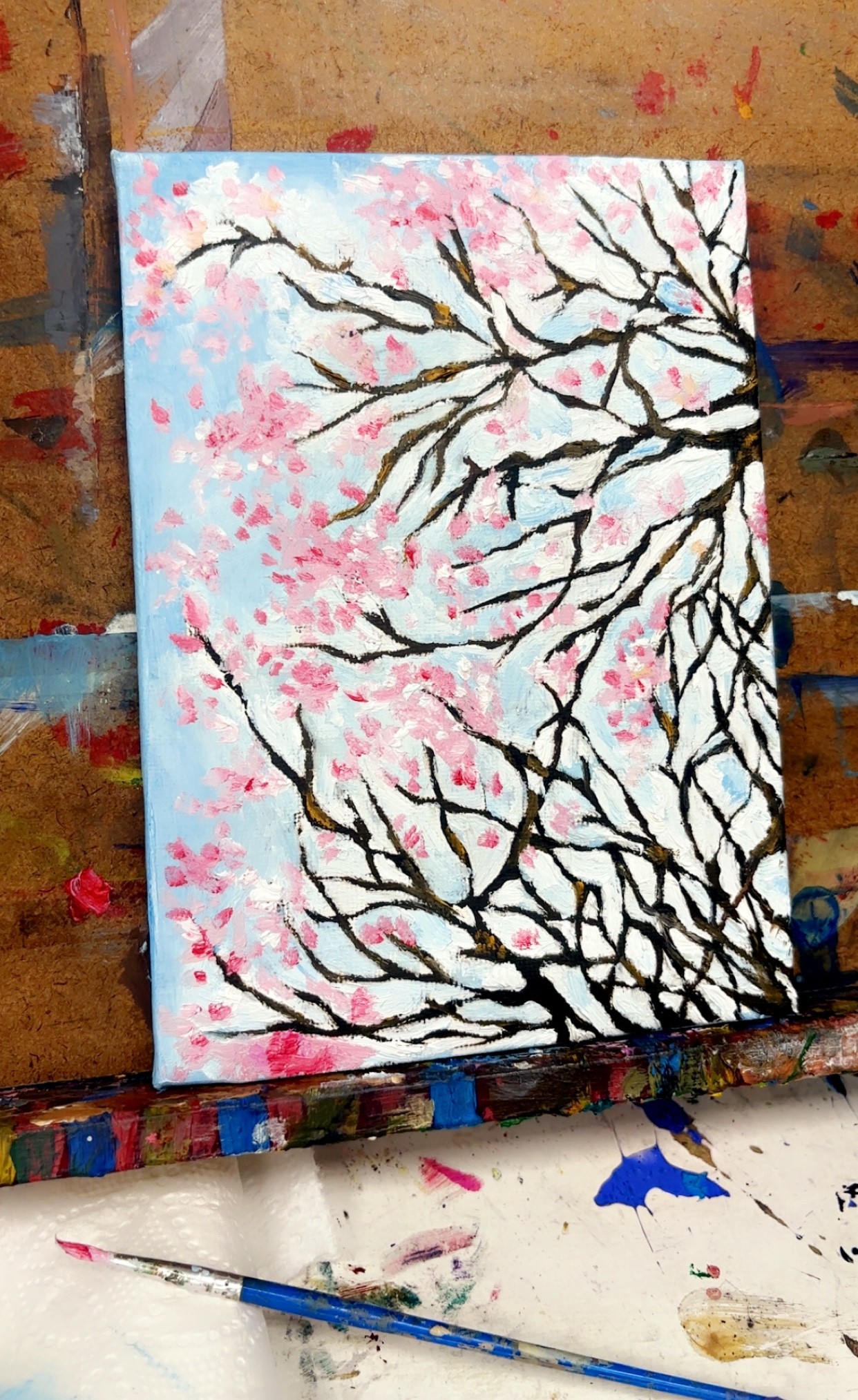 An oil painting of cherry blossom branches against a pale blue sky