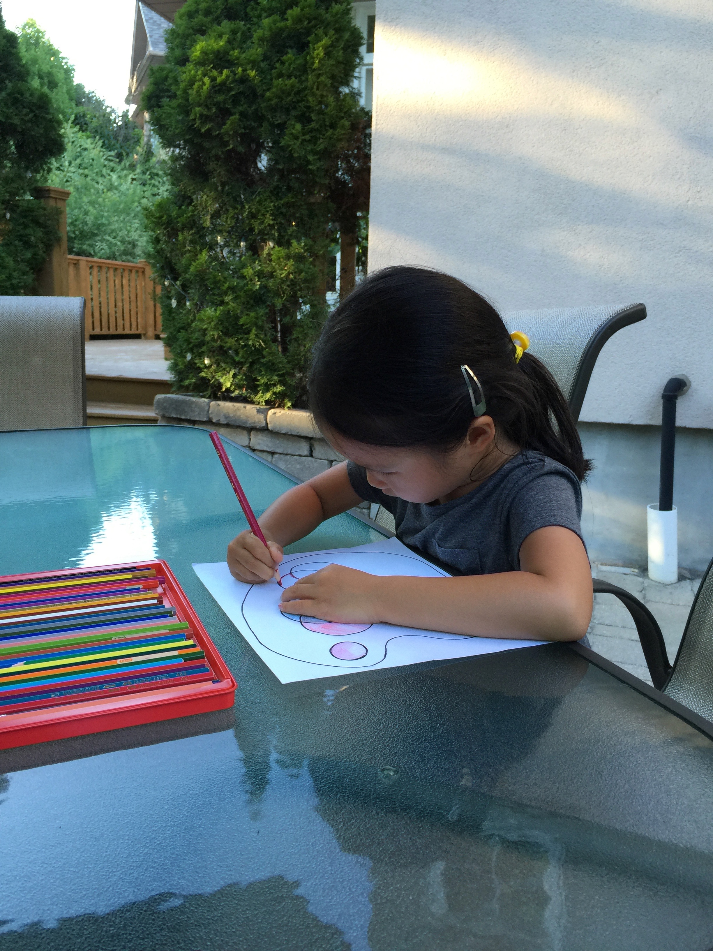 A young Mia drawing with colored pencils at an outdoor patio table