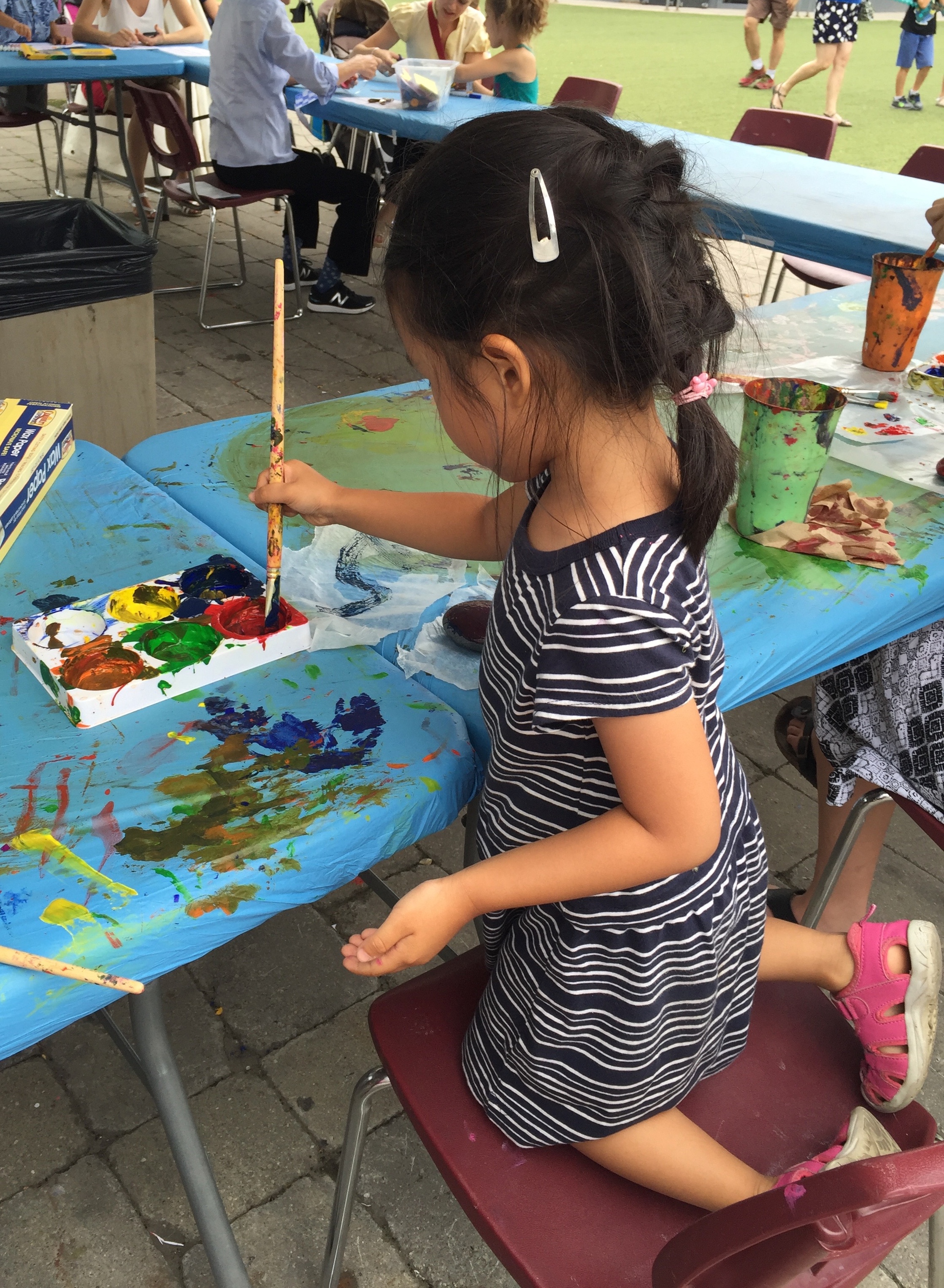 A young Mia painting at a table during an outdoor community art event