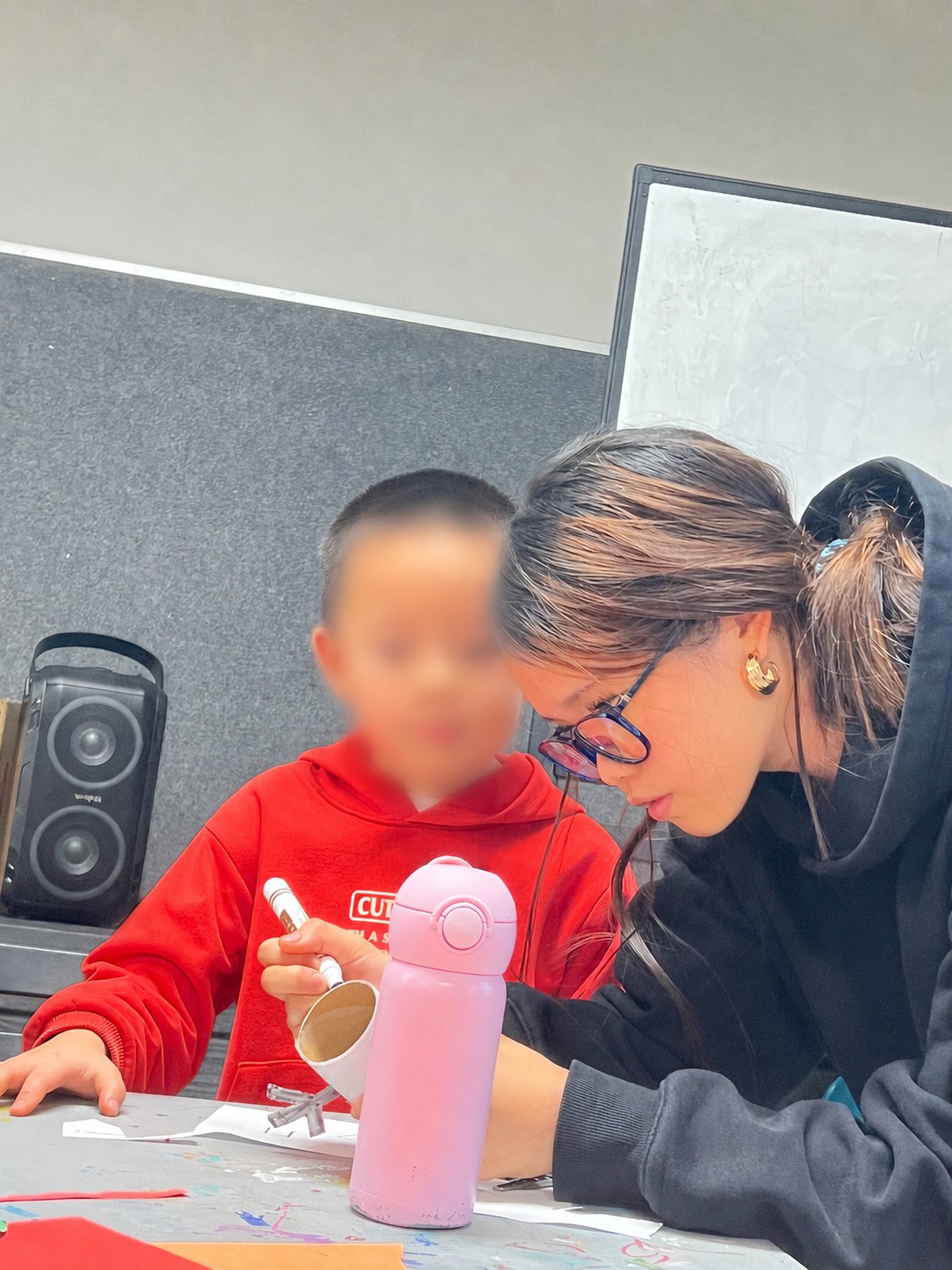 Mia helping a child in a red hoodie with a craft activity