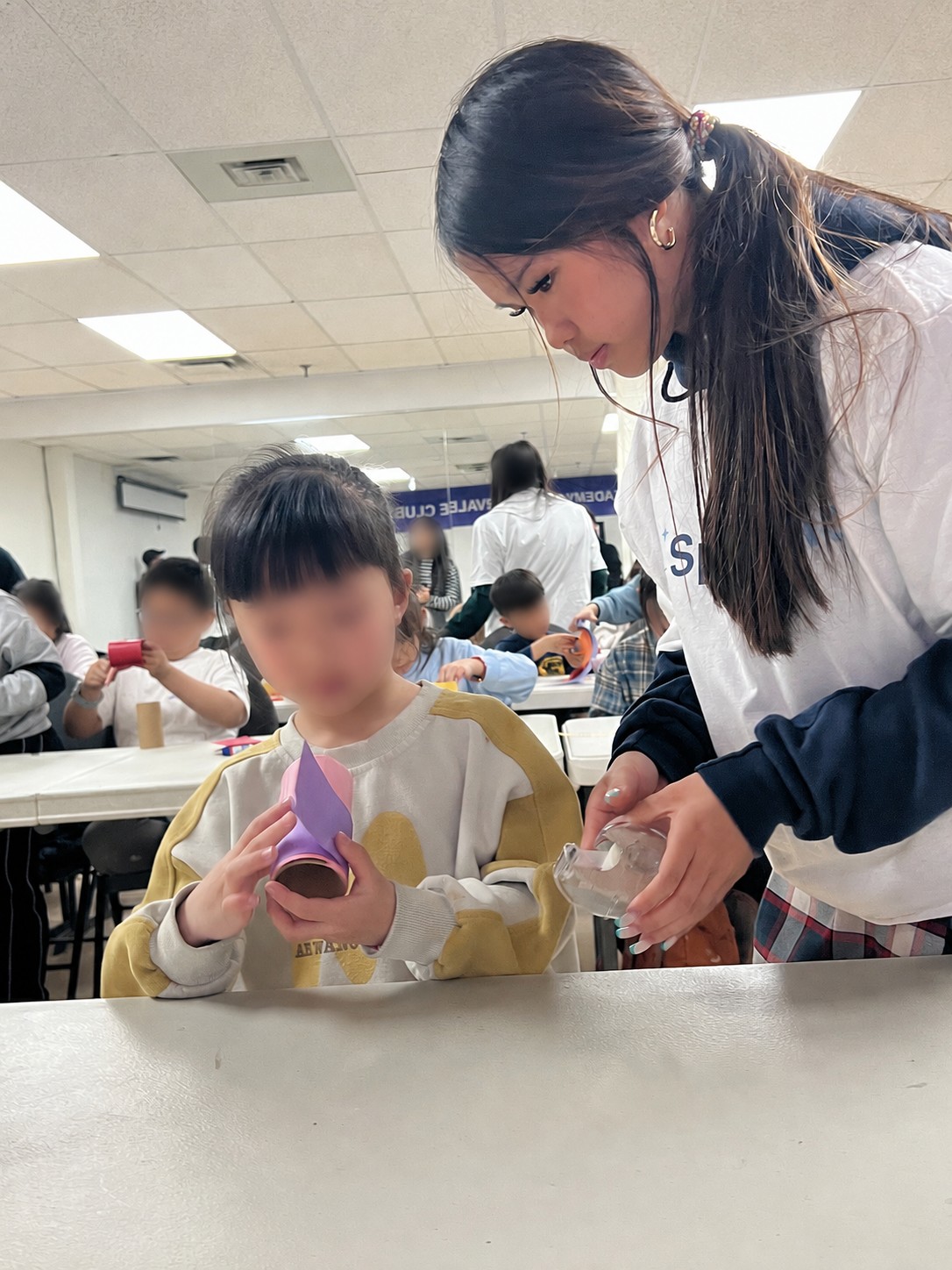 Mia helping a child with a craft activity at a table