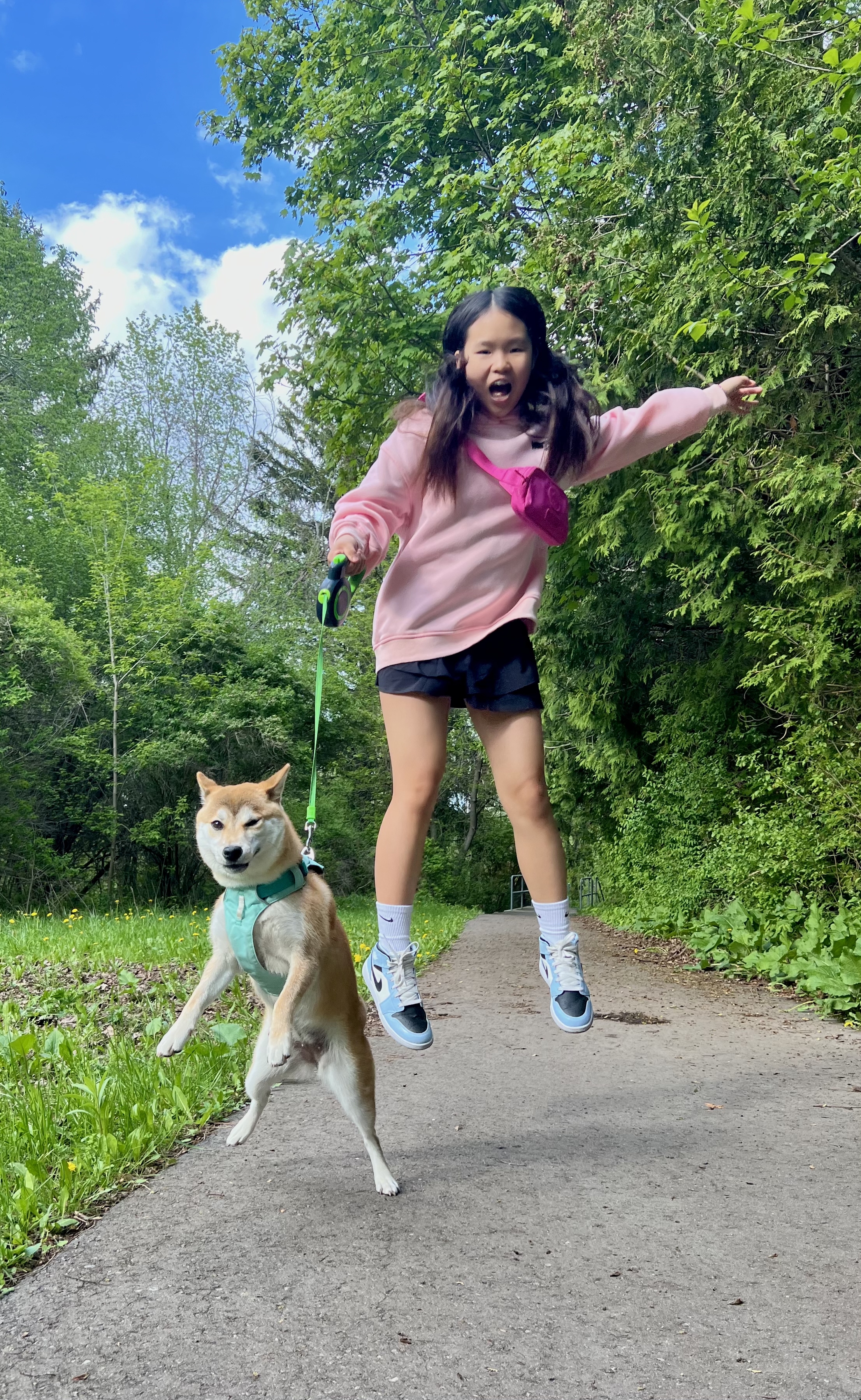 Mia jumping alongside her Shiba Inu on a wooded park trail