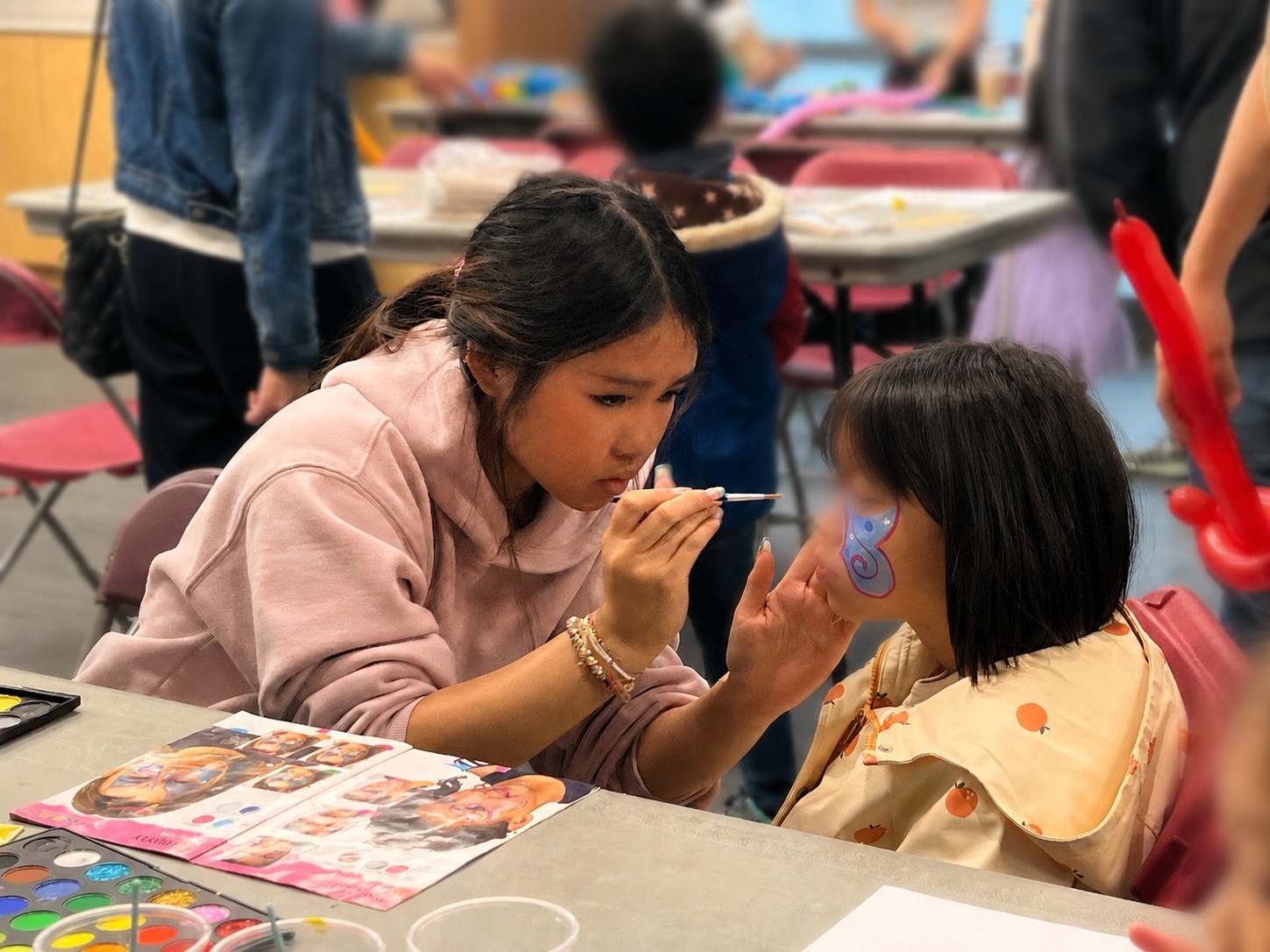Mia face-painting a child's cheek at an event table