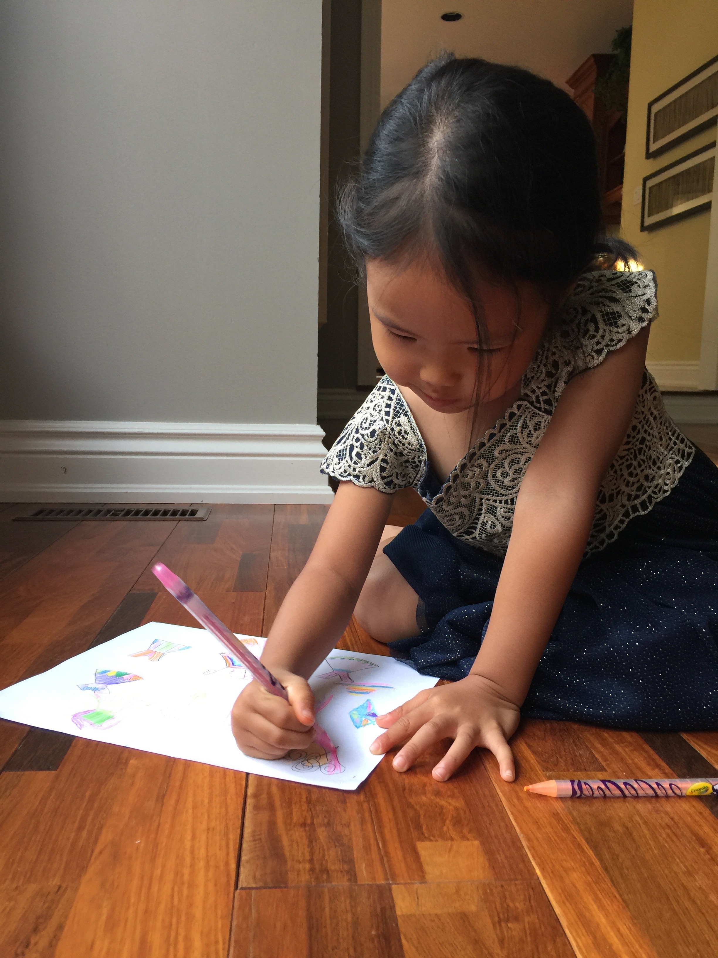 A close-up of a young Mia kneeling on the floor coloring a drawing