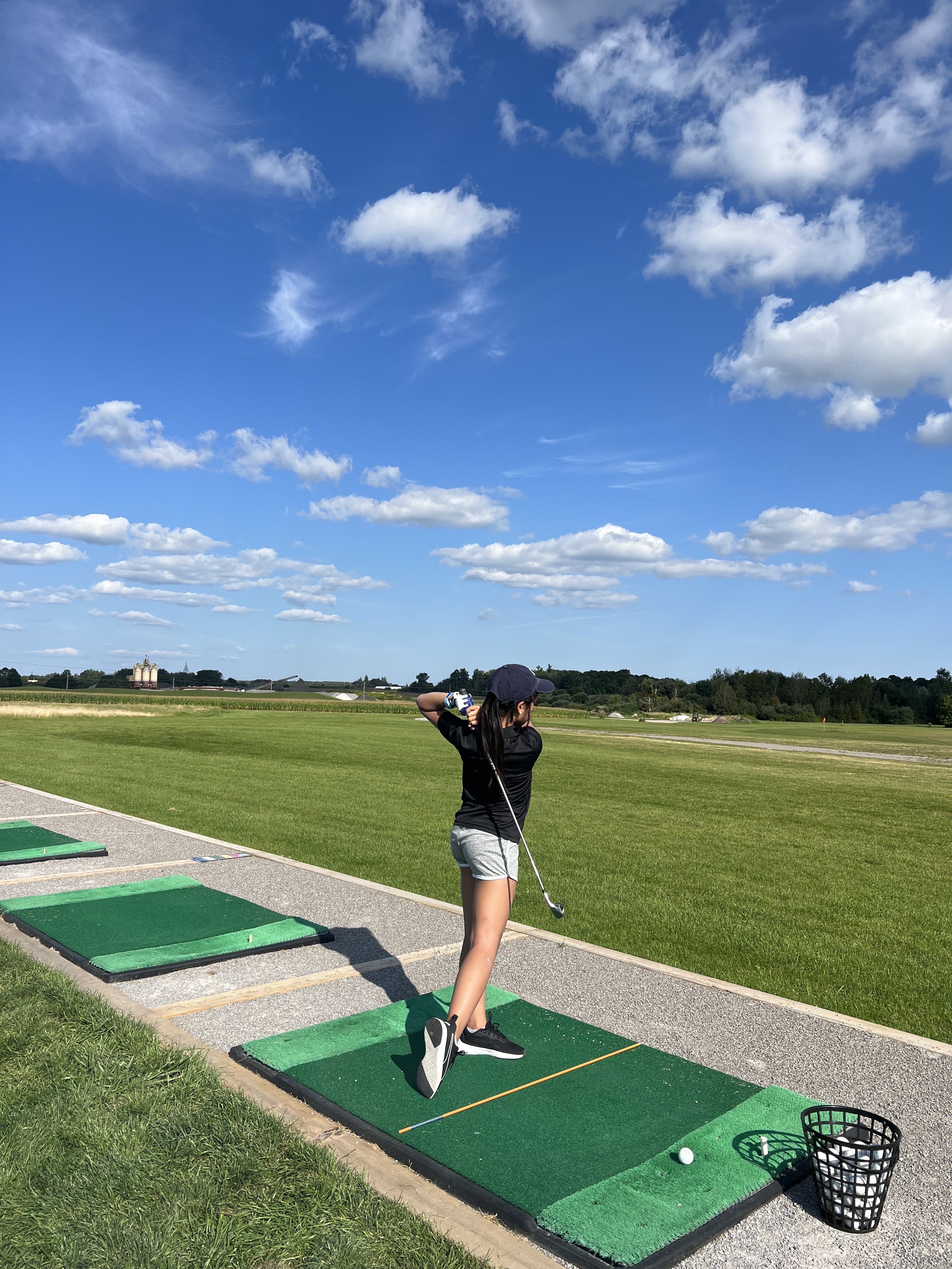 Mia completing a golf swing follow-through at a driving range