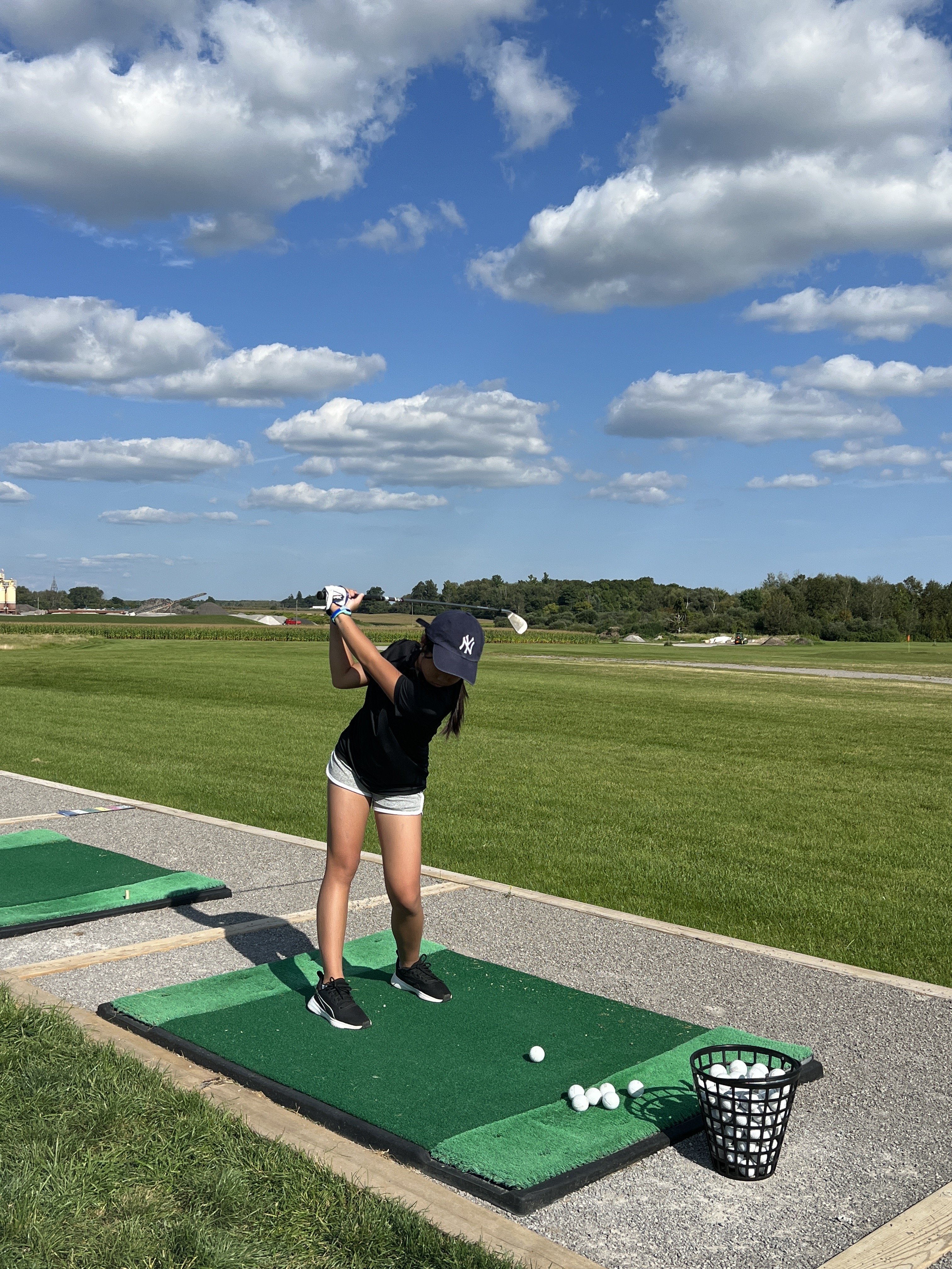 Mia mid-swing at a golf driving range on a sunny day