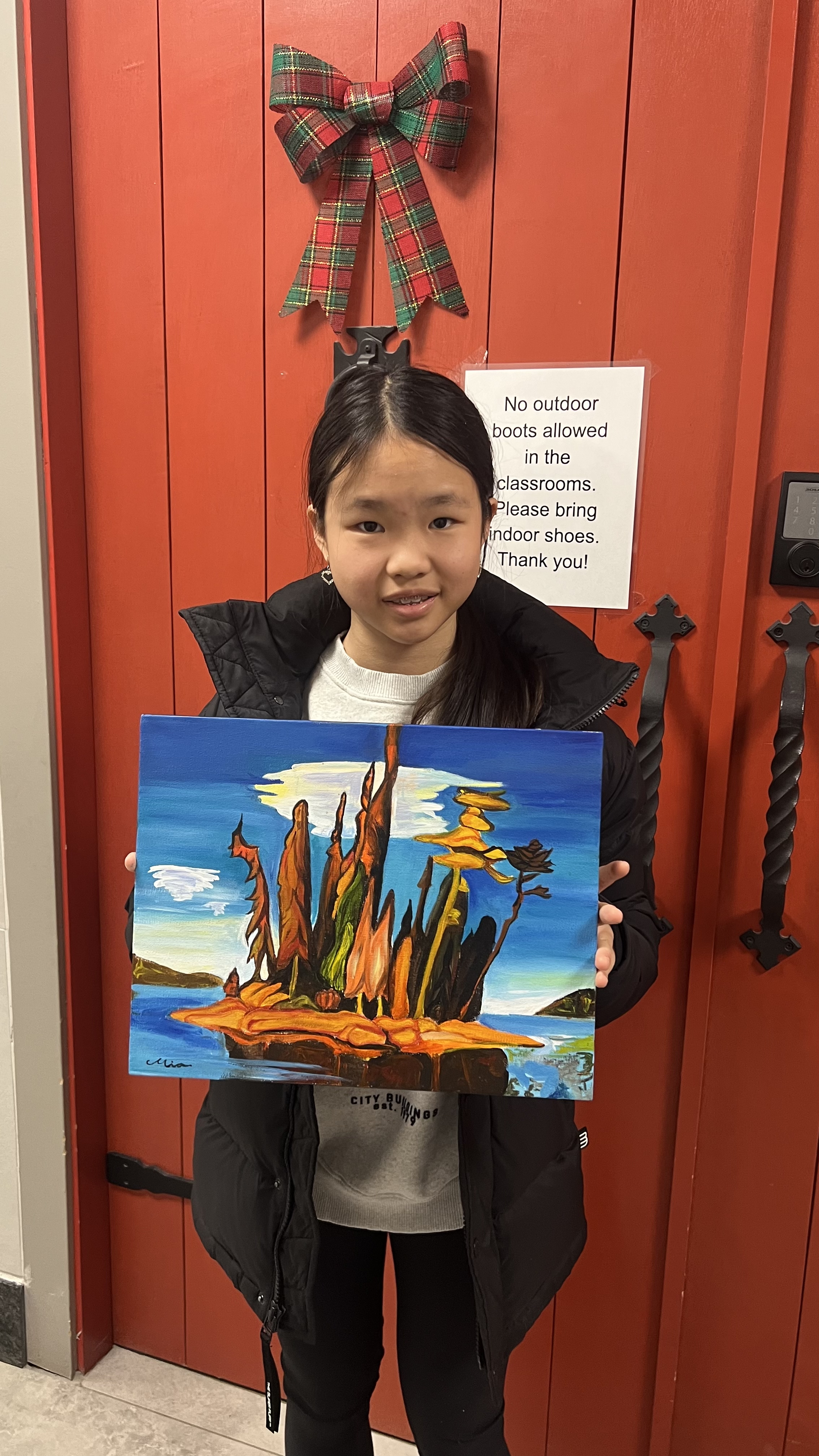 A young Mia holding her painting of windswept pine trees on a rocky island