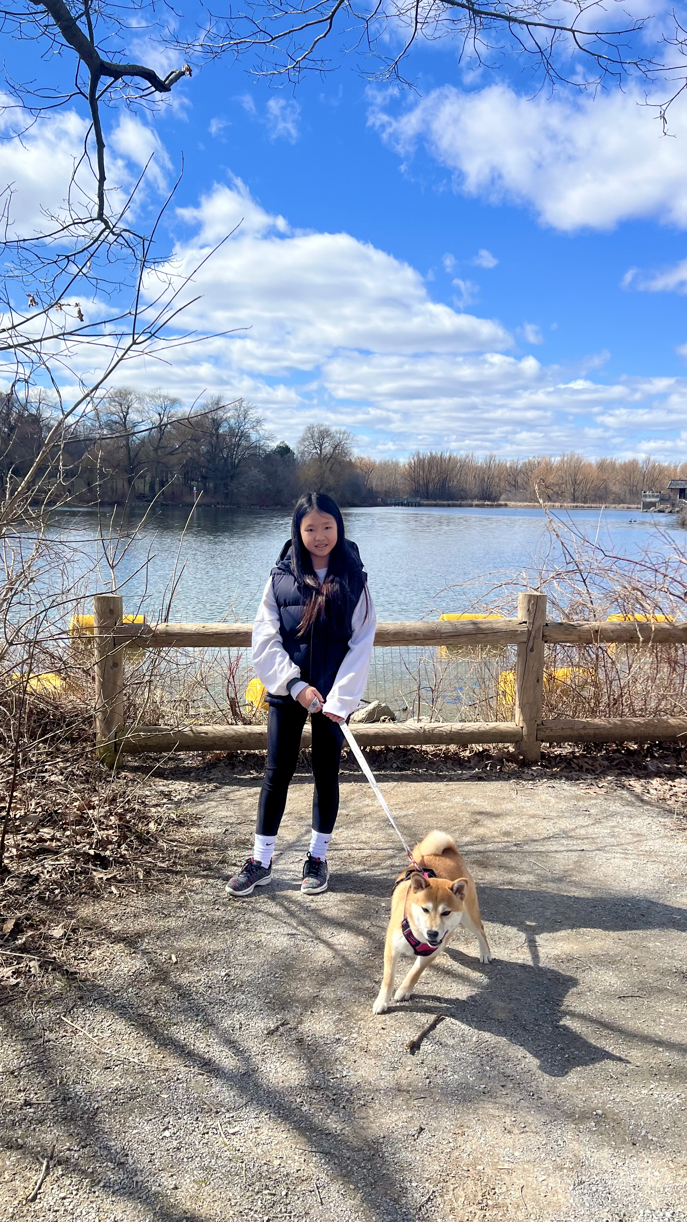 Mia walking her Shiba Inu on a trail beside a lake
