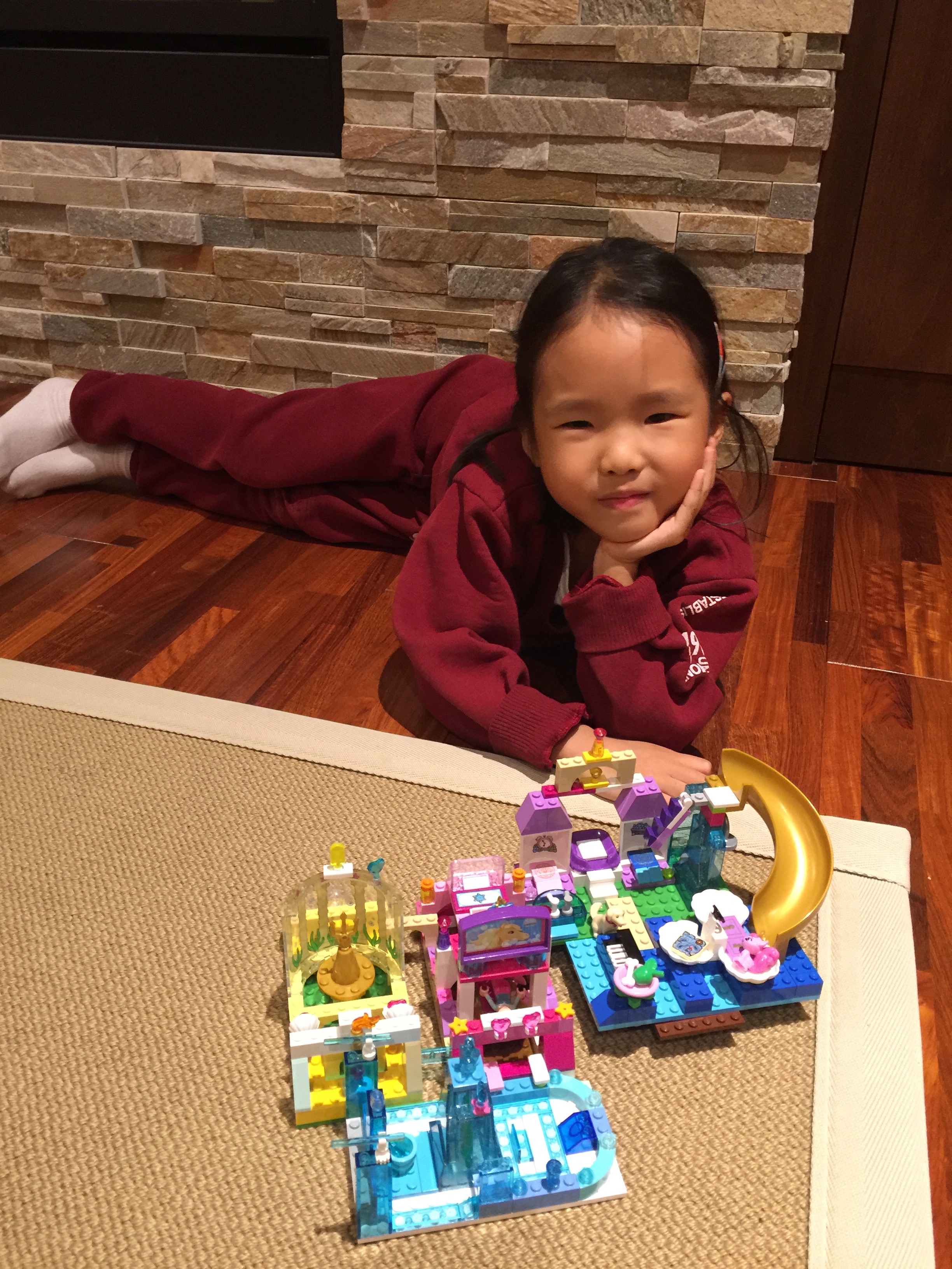 A young Mia lying on the floor next to a Lego Friends set she built