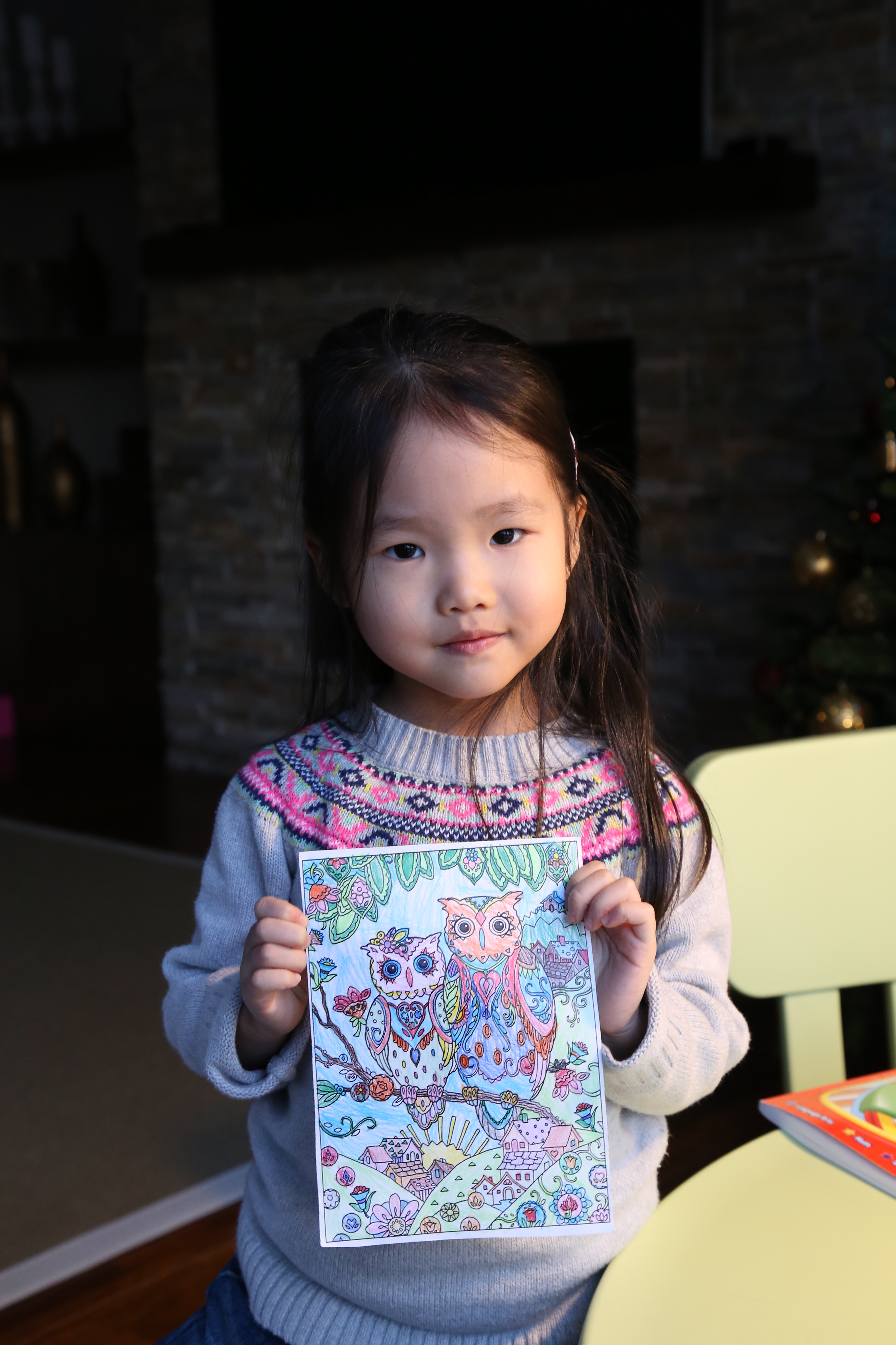 A young Mia holding a detailed coloring page of two owls that she colored in