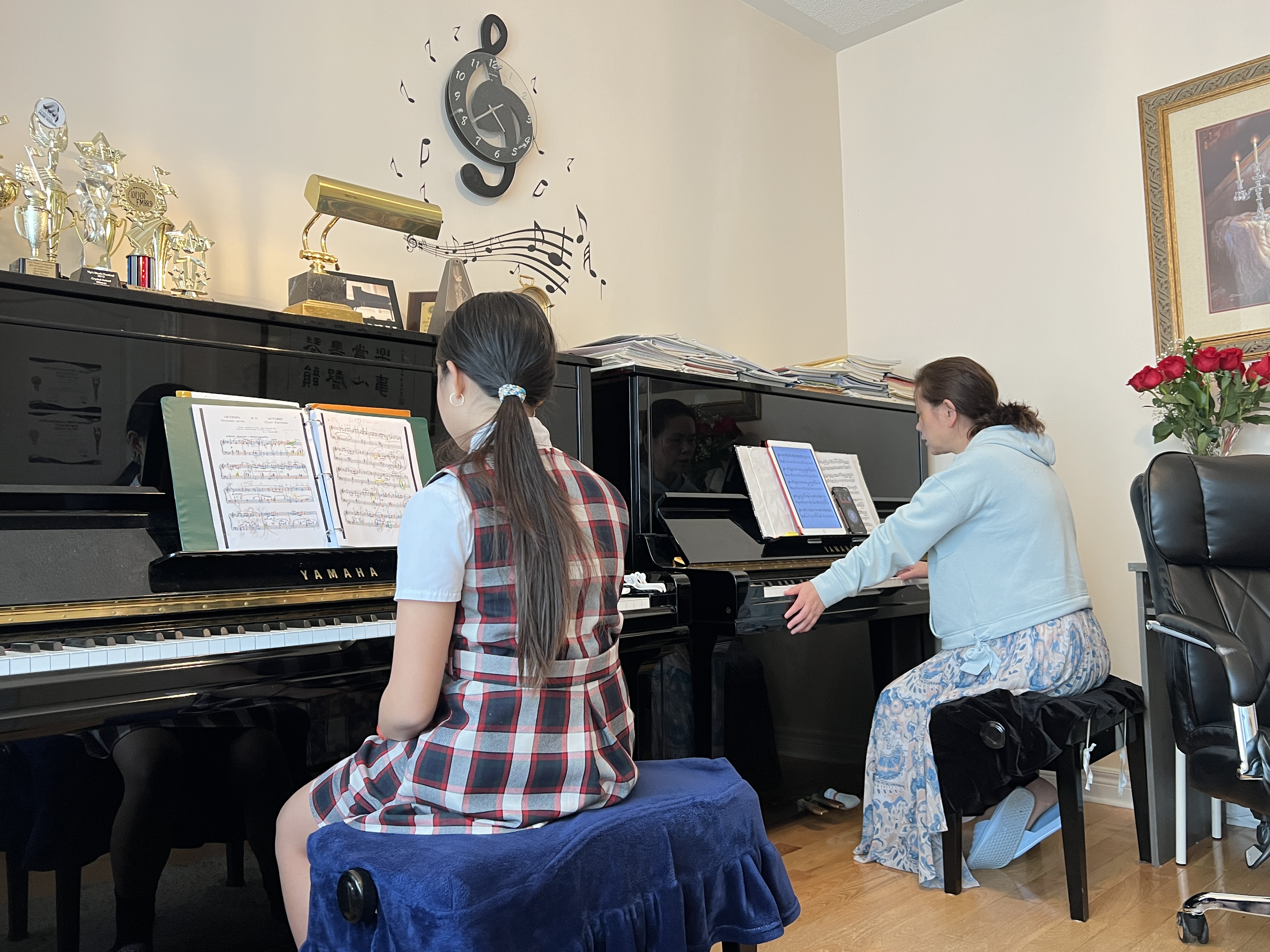 Mia at the piano during a lesson at home, with music trophies on the piano behind her