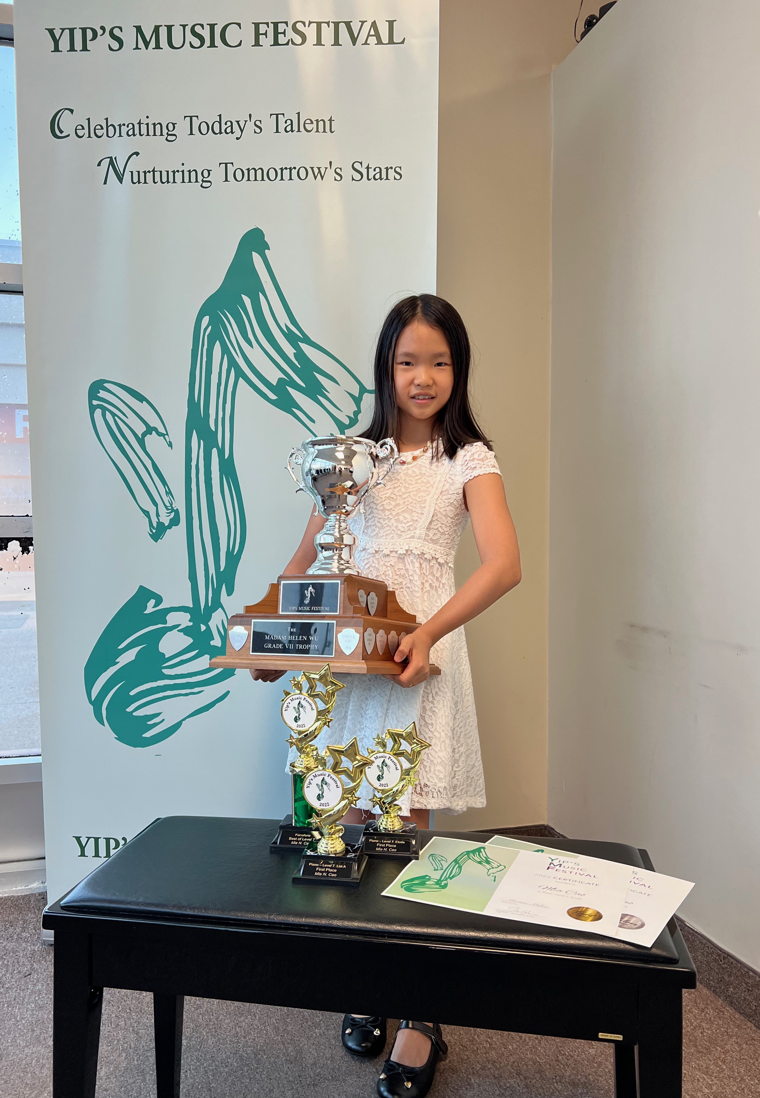 Mia holding a piano trophy and awards at Yip's Music Festival